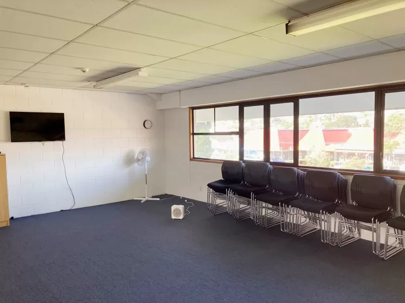 A large room showing chairs stacked along, under the windows