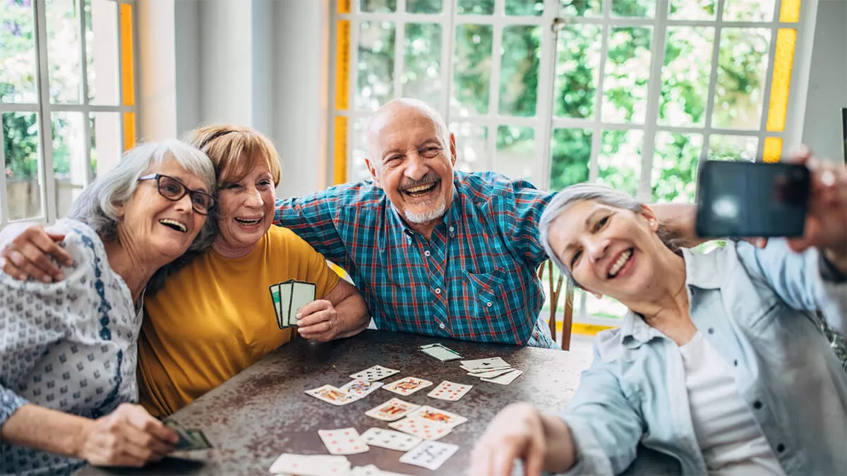 Four people older in age are sitting around a table happily playing a game of cards.