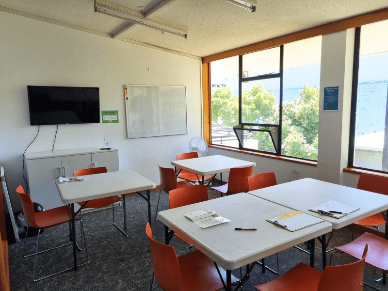 Mostly full view of room 3 with tv and whiteboard on the wall, 4 tables and chairs in the middle of the room and big windows on the right side