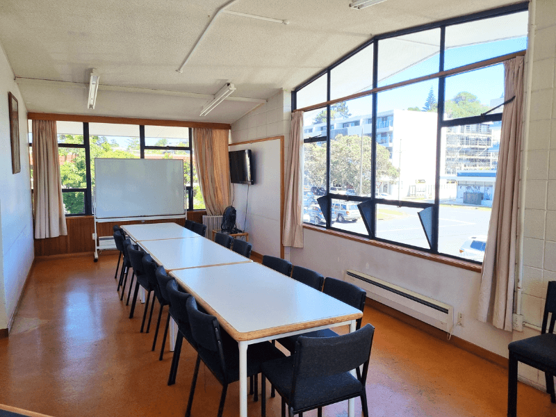 Full view of meeting room 1 at Heart of the Bays. Windows, chairs and long tables with white board in the background